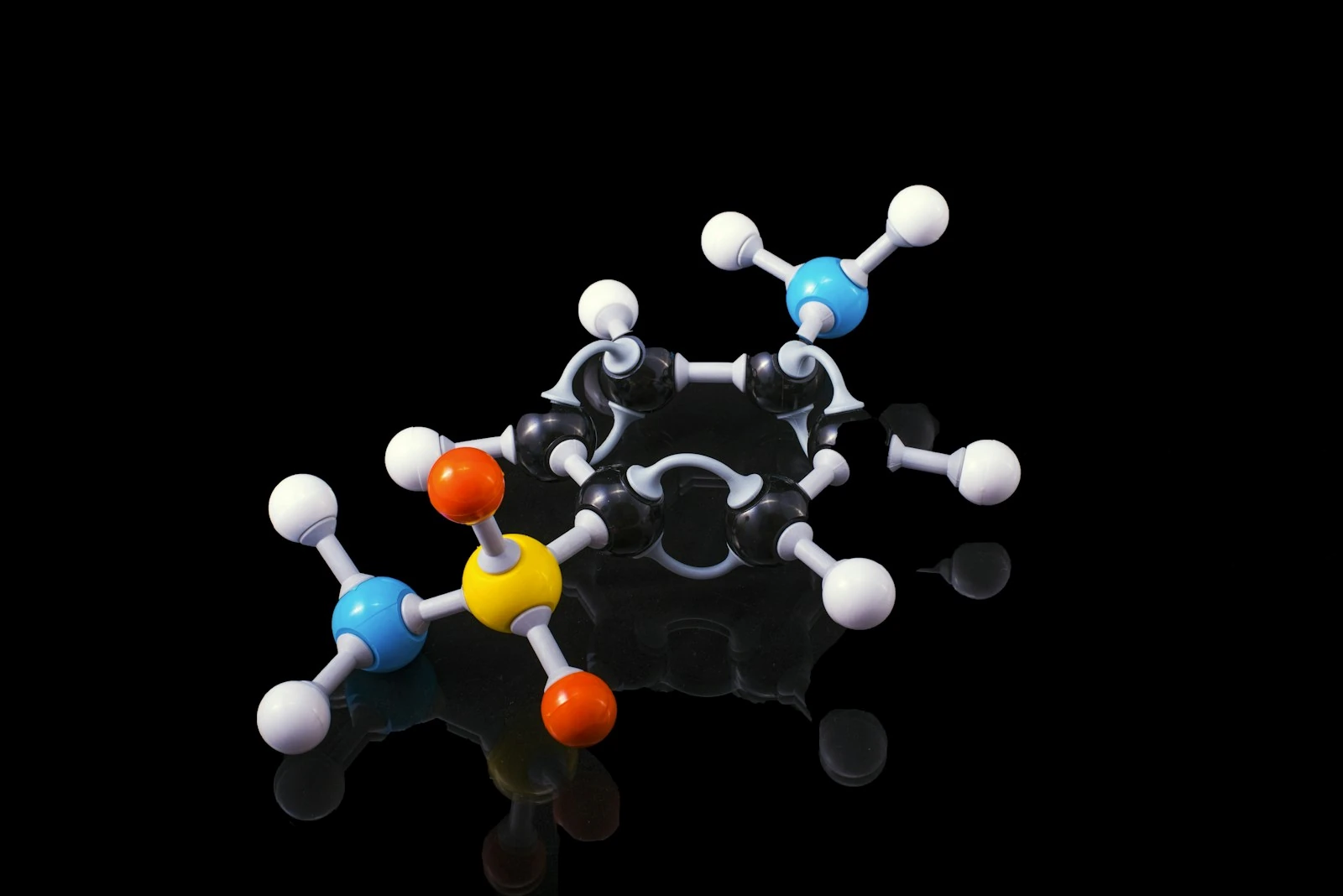 A molecule model with reflection on a dark surrounding. Sulfanilamide if someone is really interested !!Sulfanilamide was a medicine used to treat streptococcal infections. One  version of the drug, in liquid form, was introduced in the market after  having being tested only for flavor, appearance and fragrance but not for toxicity. It caused the deaths of more than 100 people back in 1937. As we are all awaiting the cure for COVID19 let his be a reminder of what untested, unsafe and "rushed to market" drugs can do to people.. Photo by Terry Vlisidis, Unsplash.